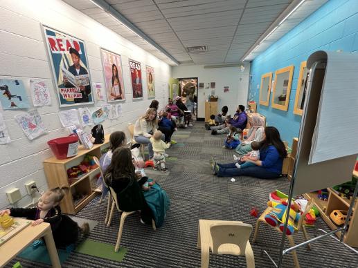 A photo of the Park Place Library KidZone where adults and children are attending a If You Give A Mouse a Cookie character visit. There are posters on the walls and toys everywhere.