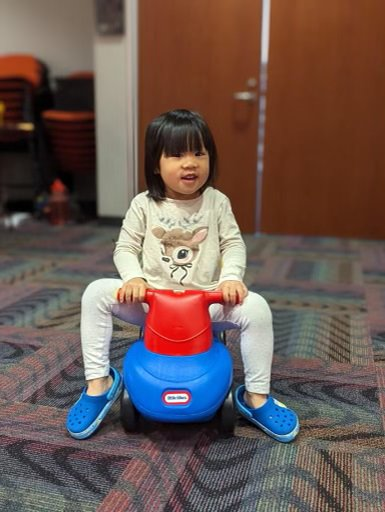 a toddler girl sitting on a blue and red push toy