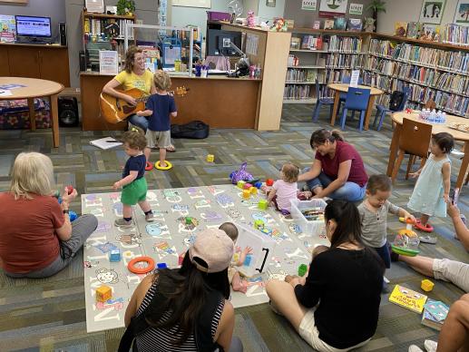 Families gathered together on the rug with learning toys and books.