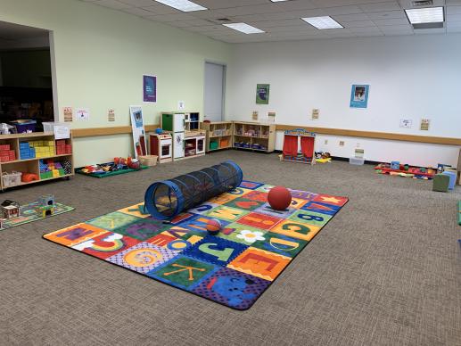 The large meeting room at the Stella Link library, set up for the Family Place Play Series. There are numerous toys spread throughout the room, including blocks, a play kitchen, a puppet theater, dolls, puzzles, cars, and more.