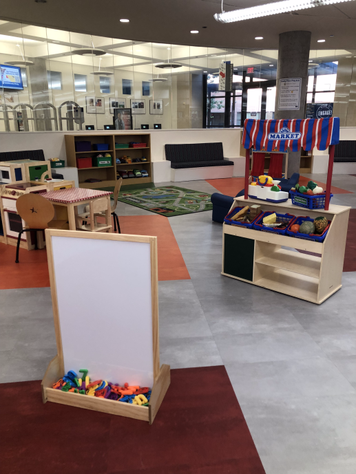 a brightly colored indoor play area for kids, with a magnet board, a farmers market stall, and a wooden kitchen