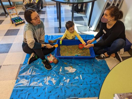 Mother is talking to staff while they play with child in sensory bin