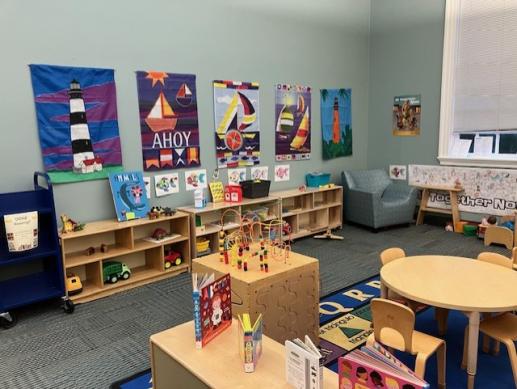 A KidZone with 3 shelves of toys, a fidget cube, some books, a short table and chairs and an adult chair