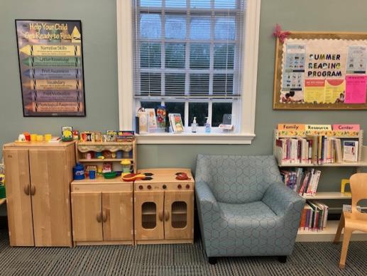 A play refrigerator, pantry, and stove with play food and pots and pans and dishes, an adult chair, and a family resource center